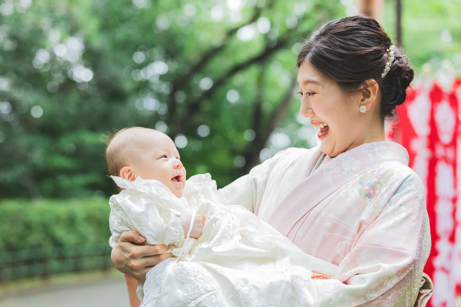 お宮参りでママに抱っこされた赤ちゃんとママが微笑みあっている