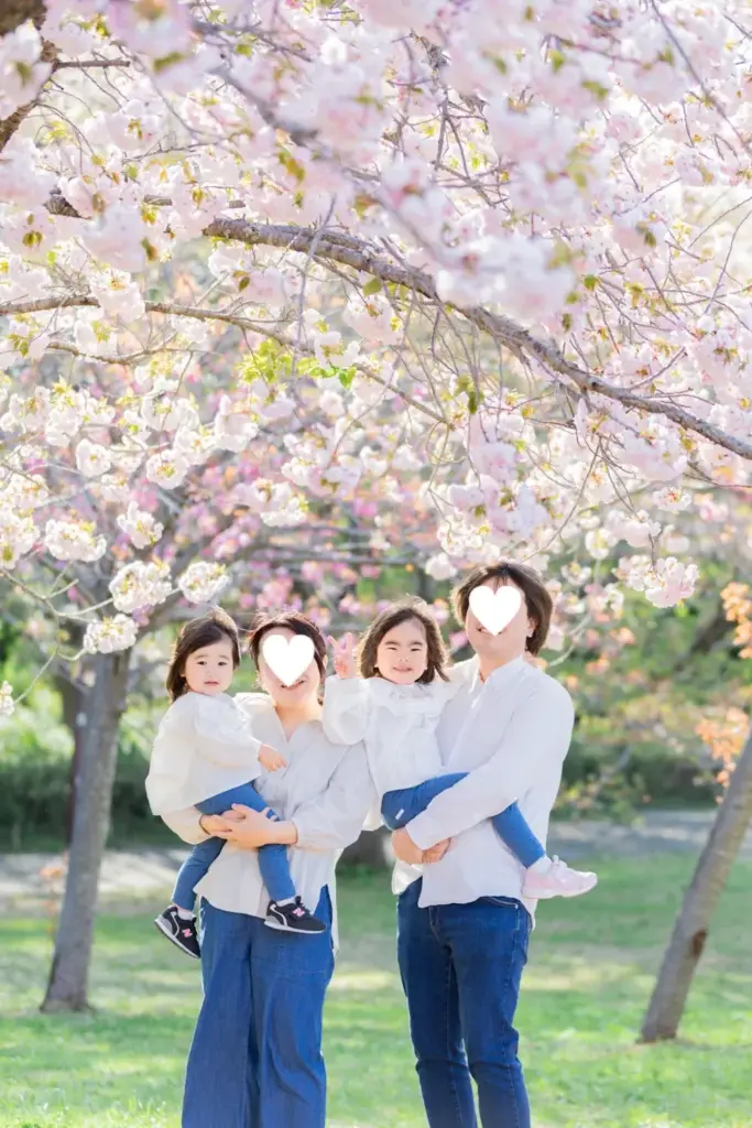 青葉の森の八重桜の下でパパとママに抱っこされている姉妹
