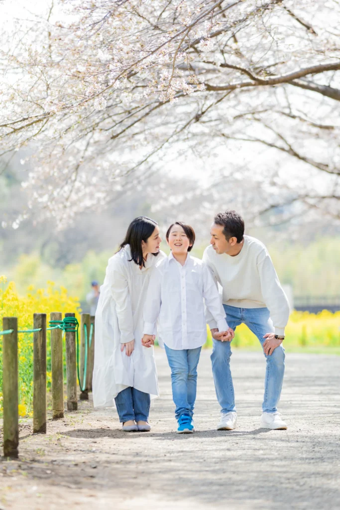 桜の下で我が子を見つめるパパとママの写真