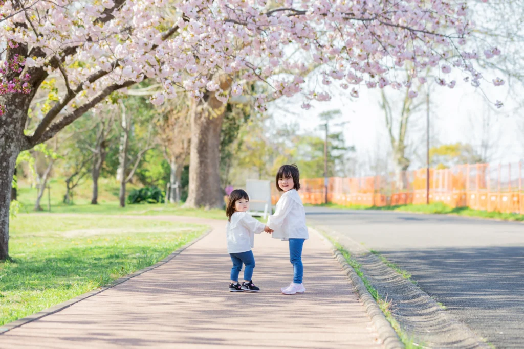 可愛いピンクの桜の下で手を繋ぐ姉妹の写真